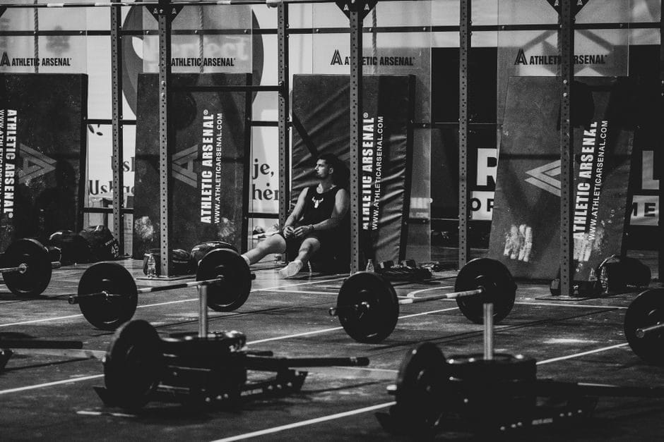 A man resting on a bench beside a loaded barbell in a gym